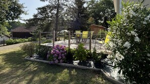 Un área exterior amurallada con terraza de madera, rodeada de plantas y árboles diversos.