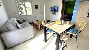 Una sala de estar moderna con un sofá, una mesa de comedor con sillas, un televisor y vistas a través de una puerta.
