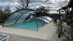 Una piscina techada con cerramiento de vidrio, rodeada por un patio empedrado y plantas en macetas.