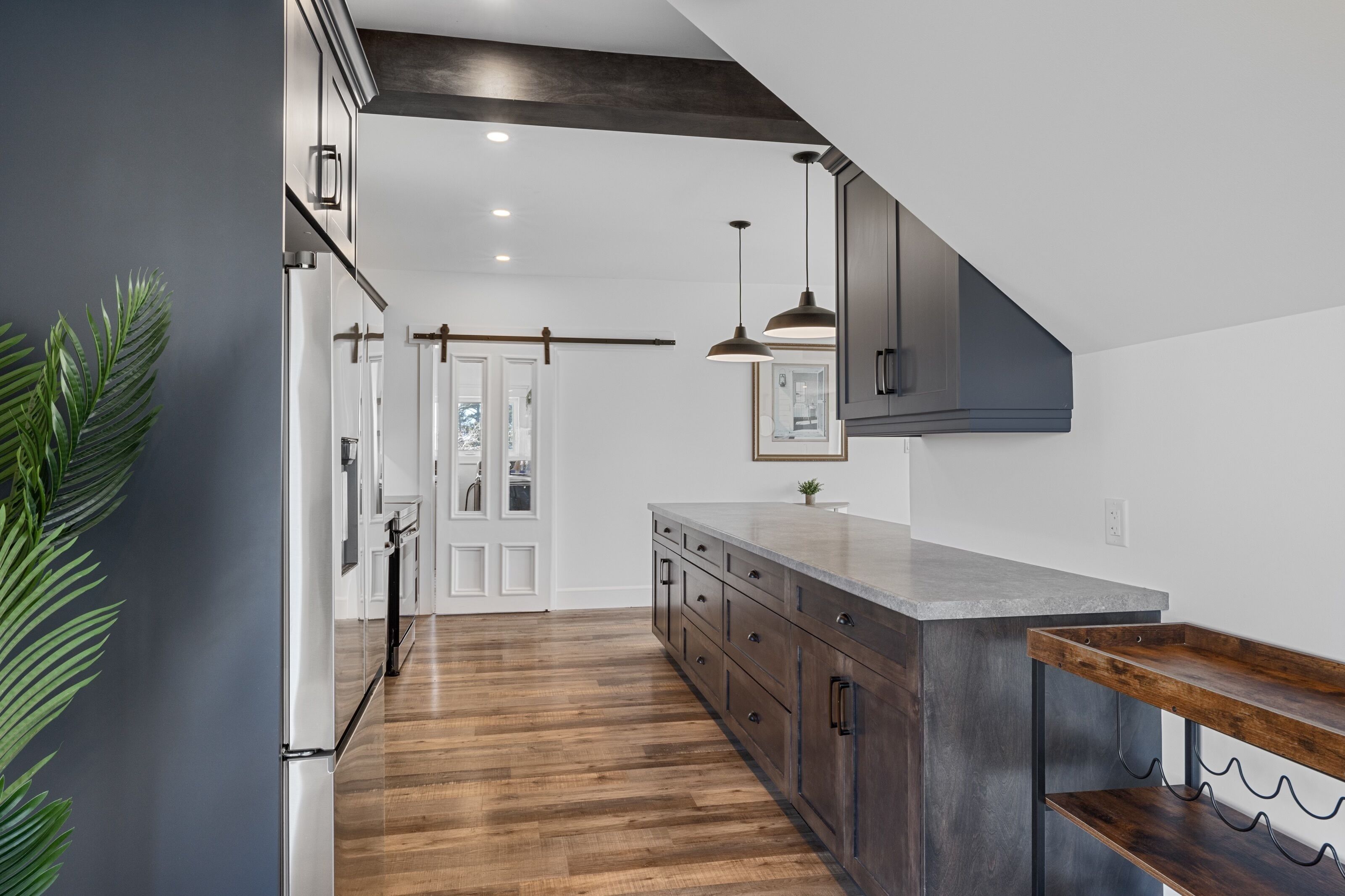 A modern kitchen with a wooden floor, dark cabinets, and pendant lighting.