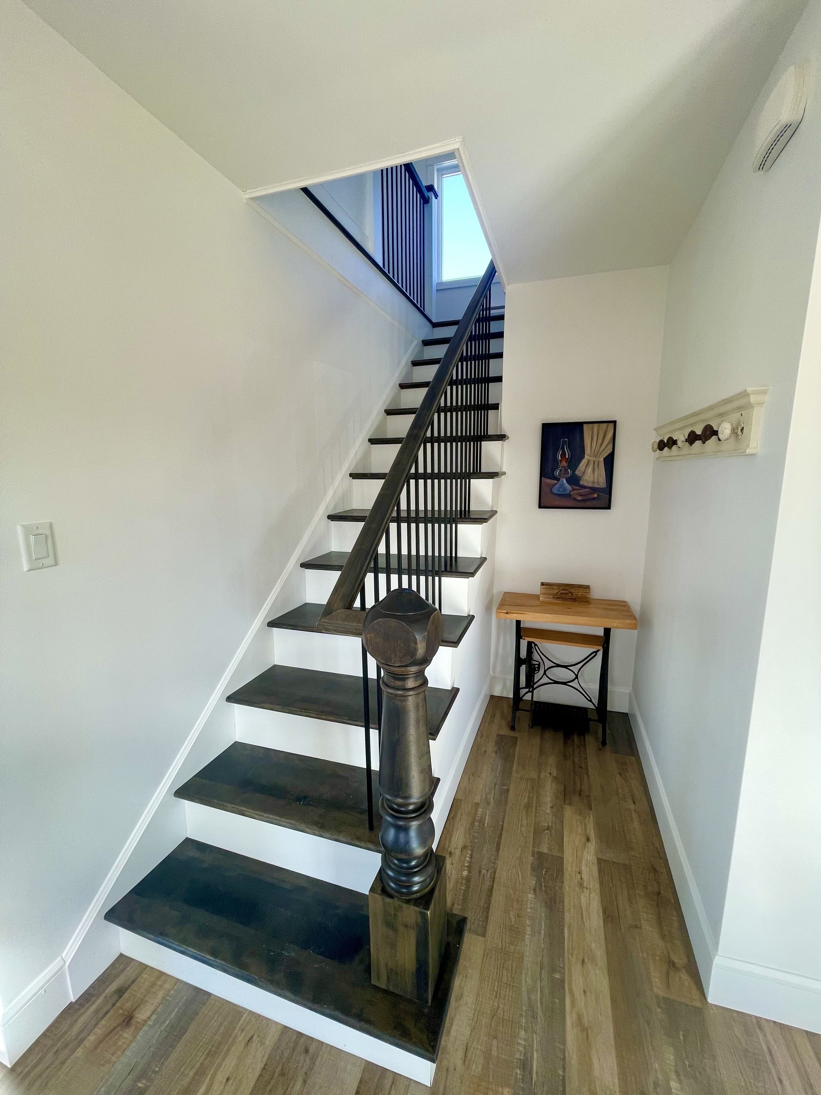 Un escalier avec des marches en bois foncé et des rampes noires, menant à l’étage supérieur.