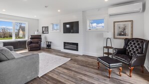 A spacious living room with a fireplace, leather armchairs, a grey sofa, and a large flat-screen TV.