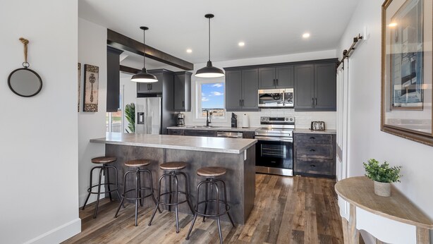 A modern kitchen with a central island, bar stools, pendant lighting, and a view of the outdoors.