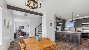 A modern kitchen with dark cabinetry, a central island with stools, and a dining area with a wooden table and chairs.