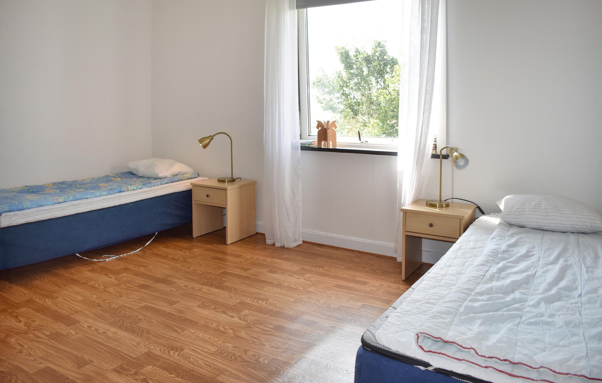 A bedroom with two beds, wooden flooring, and a window with a view of trees.