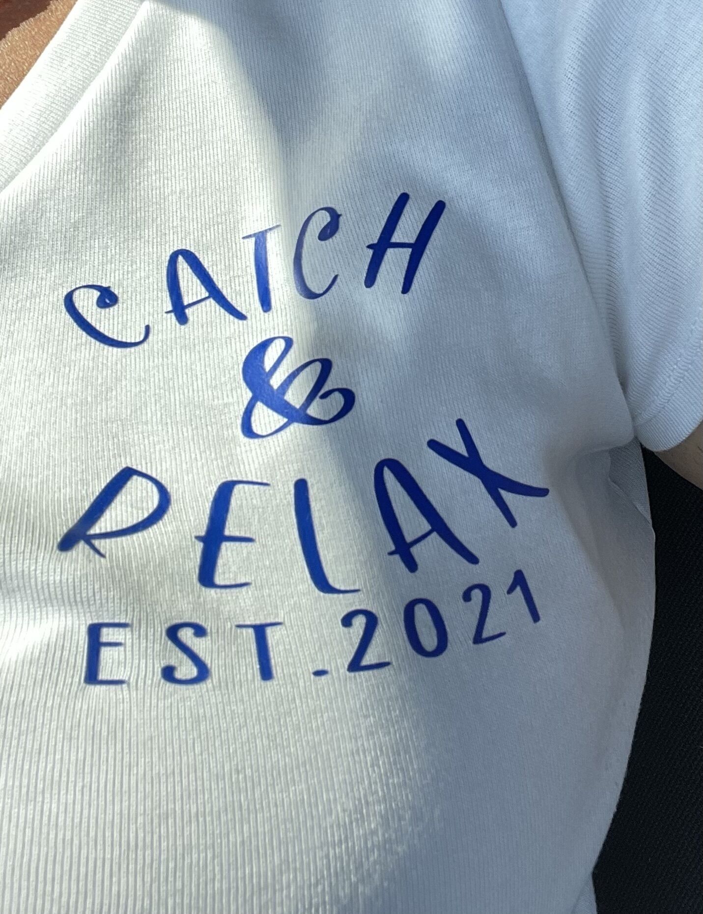A white tote bag with blue text that reads "CATCH & RELAX EST. 2021".