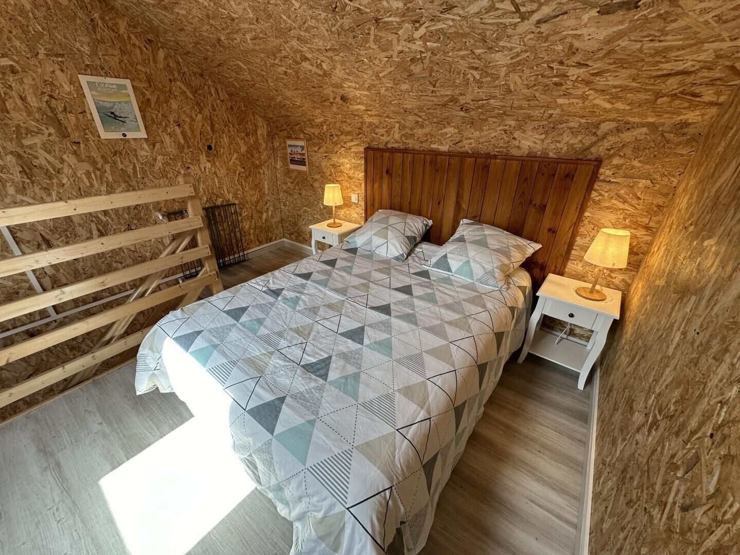 Un dormitorio con techo de madera, una cama con colcha de estampado geométrico, dos mesitas de noche con lámparas y un cabecero de madera.