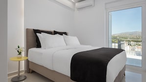 A modern bedroom with a bed, a small table with a plant, and a large window offering a view of the outdoors. - Athenian Riviera Penthouse Apartment (Vari)