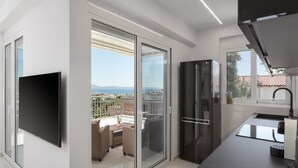 A modern kitchen with a large window, a flat-screen TV, and a balcony with outdoor furniture. - Athenian Riviera Penthouse Apartment (Vari)