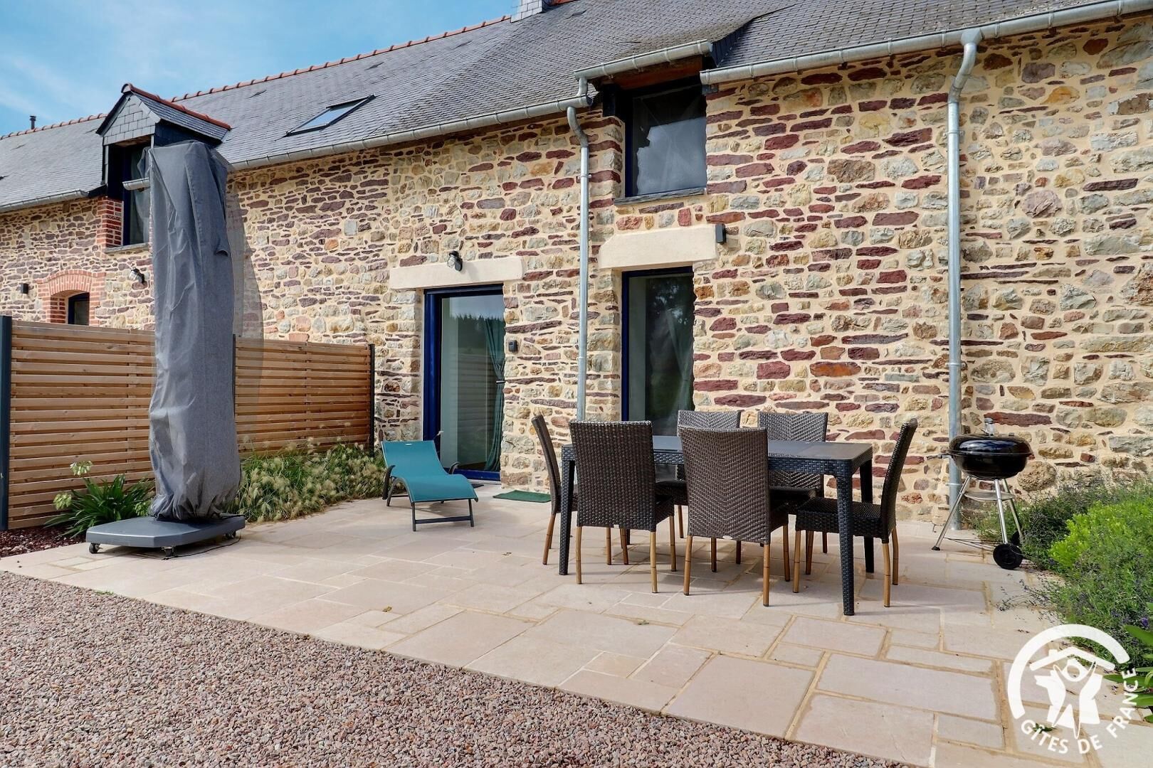 A stone house with a patio, outdoor seating, and a covered sculpture.