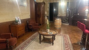 Ein traditionell eingerichtetes Wohnzimmer mit Holzboden, einem gemusterten Teppich, einem Couchtisch mit dekorativen Gegenständen, einem roten Sessel, einer Holzkommode und einer Treppe im Hintergrund.