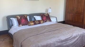 A bedroom with a large bed, a wooden wardrobe, a patterned rug, and a framed picture on the wall.
