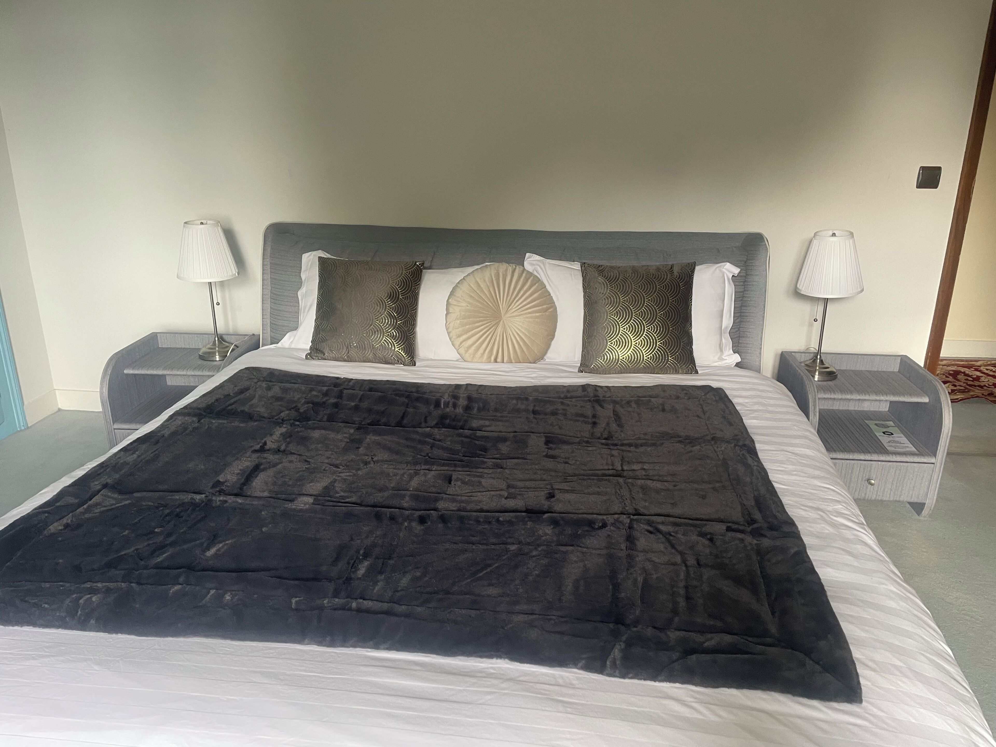 A neatly made bed with a black bedspread, two bedside tables with lamps, and decorative pillows.