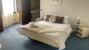 A neatly made bed with a beige blanket and pillows, a bedside table with a lamp, and a framed picture on the wall.