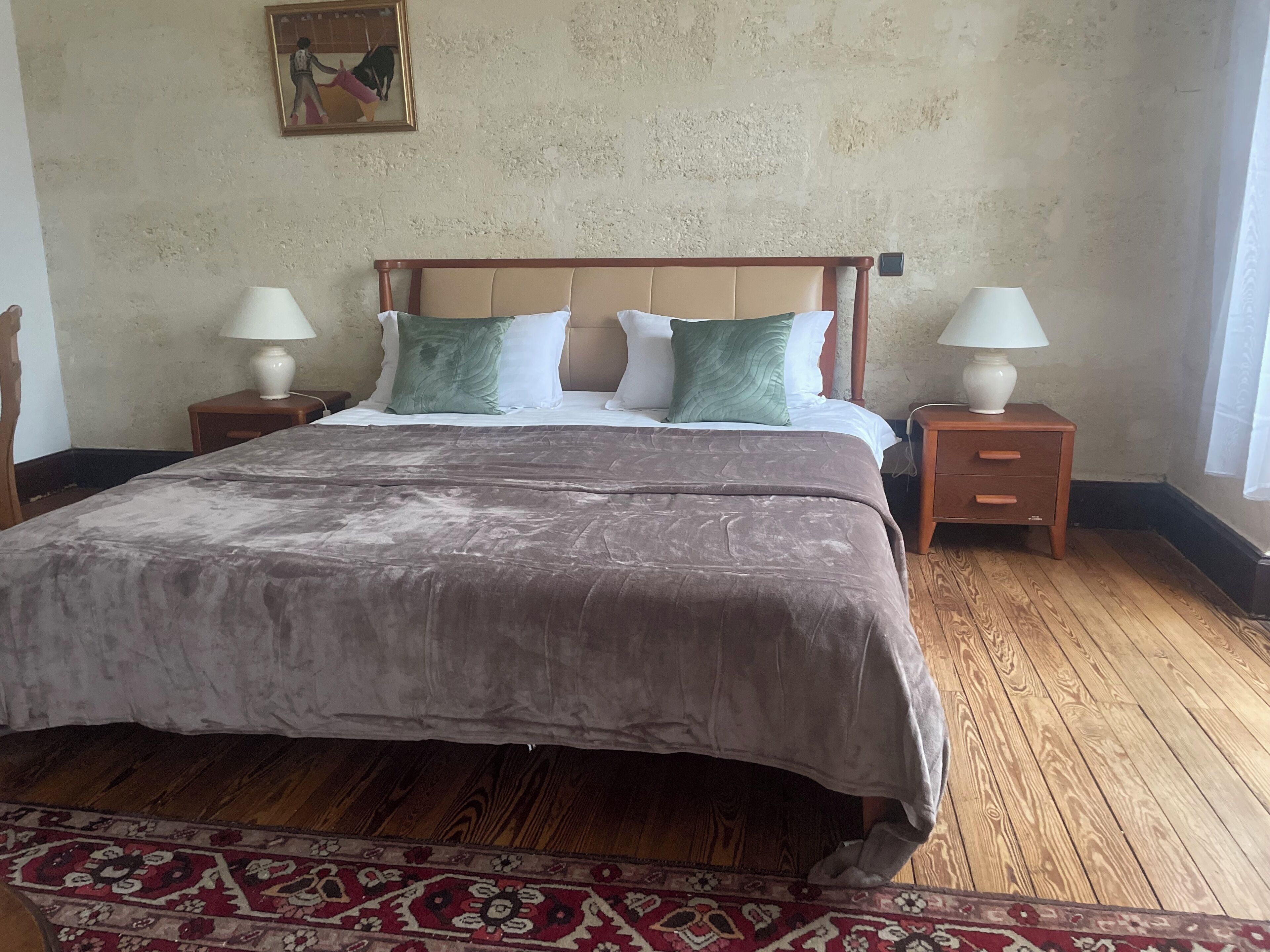 Ein Schlafzimmer mit einem großen Bett, zwei Nachttischen mit Lampen, einem gemusterten Teppich und einem Bild an der Wand.