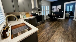 Een moderne keuken met grijze kastjes, roestvrijstalen apparatuur en een eethoek met houten lambrisering.