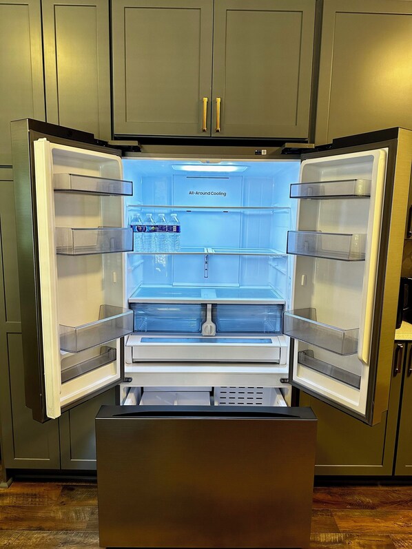 An open refrigerator with clear shelves and a water dispenser.