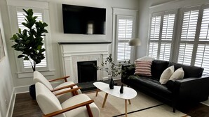 Een moderne woonkamer met een open haard, een zwarte leren bank, een witte fauteuil en een salontafel.