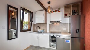 Eine kleine Küche mit weißen Schränken, einem Edelstahl-Kühlschrank, einem Geschirrspüler und einem Fenster mit Blick nach draußen.