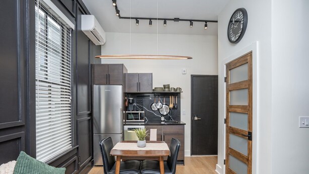 Una cocina compacta con electrodomésticos modernos, una zona de comedor con mesa y sillas, y un ventanal con persianas.