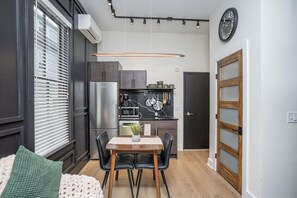 A compact kitchen with modern appliances, a dining area with a table and chairs, and a large window with blinds. - Sleek & Cozy 1st Flr Flat- Walk to Brown & Wayland (Providence)