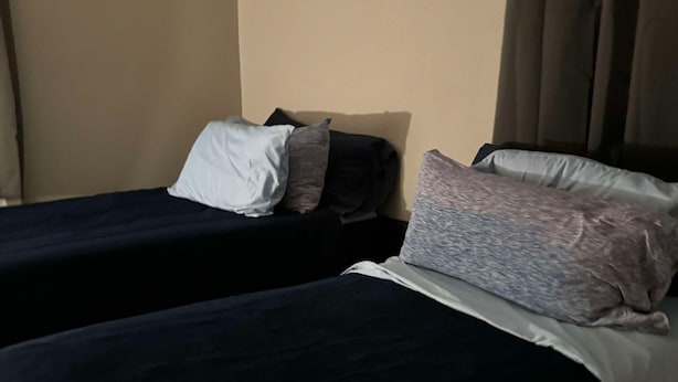 Et hotelværelse med to enkeltsenge, hver med et mørkt sengetæppe og puder.