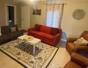 A living room with a red sofa, a white coffee table, a patterned rug, and a brown armchair. - Beautiful Home Near Park & Museum (Silsbee)