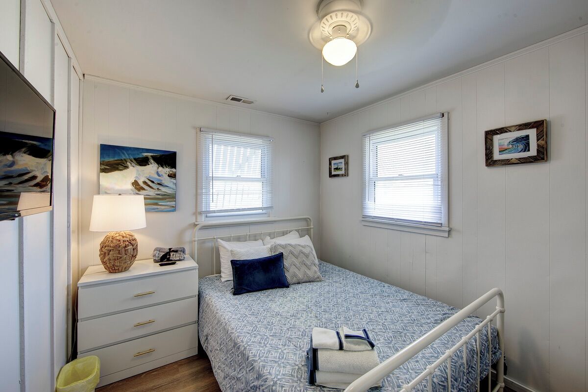 Un dormitorio con cama, mesita de noche, lámpara y una obra de arte en la pared.
