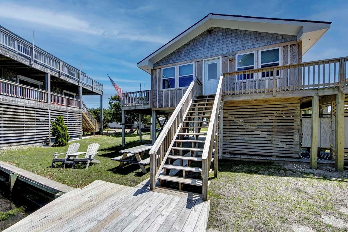 A two-story building with a wooden deck, a staircase, and a flag.