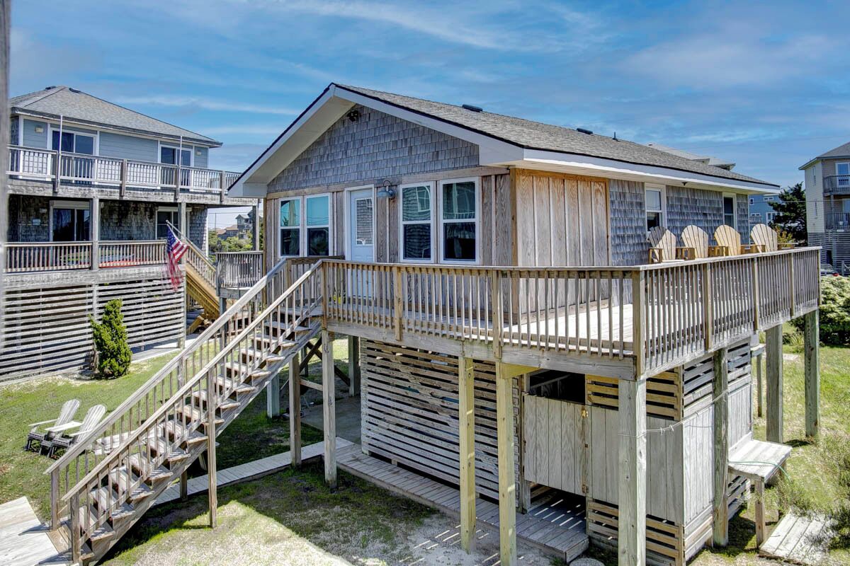 A wooden deck with a staircase leading to a covered area with windows.