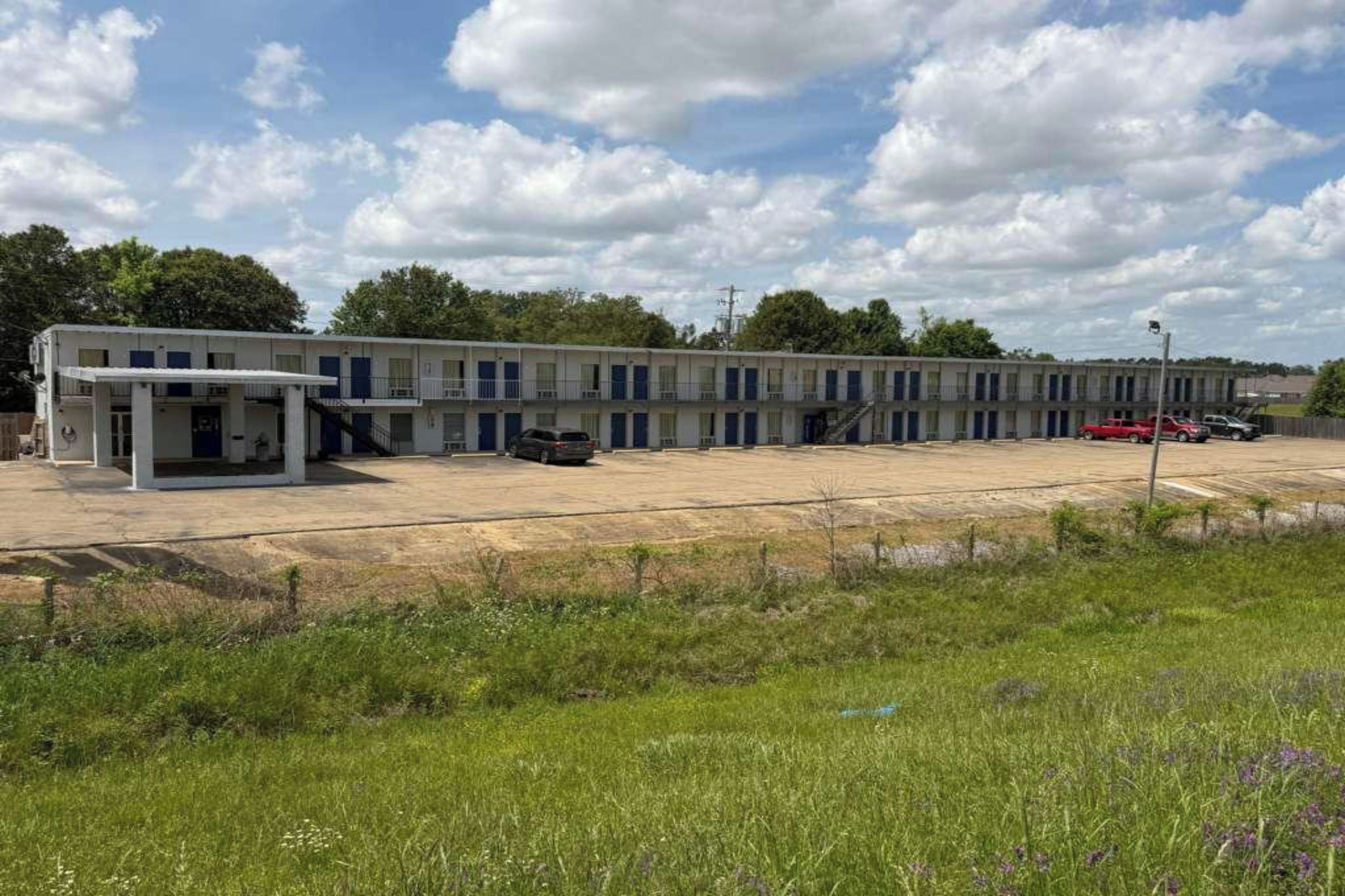 A long, single-story motel with a central entrance and a parking lot in front.