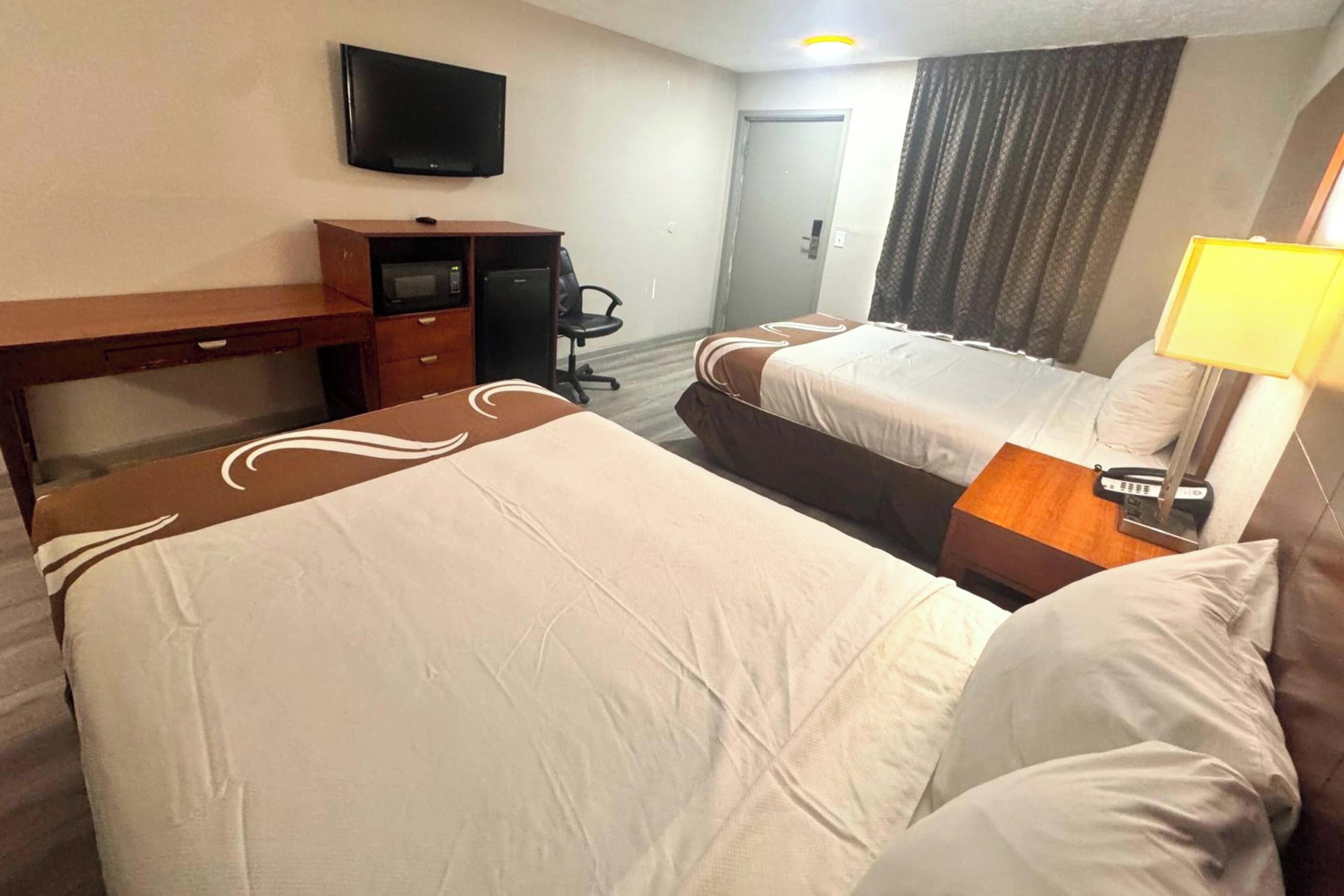 Une chambre d’hôtel avec deux lits, un bureau, une télévision et une lampe.