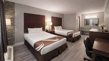 A hotel room with two beds, a desk, a chair, a mirror, and a bathroom.