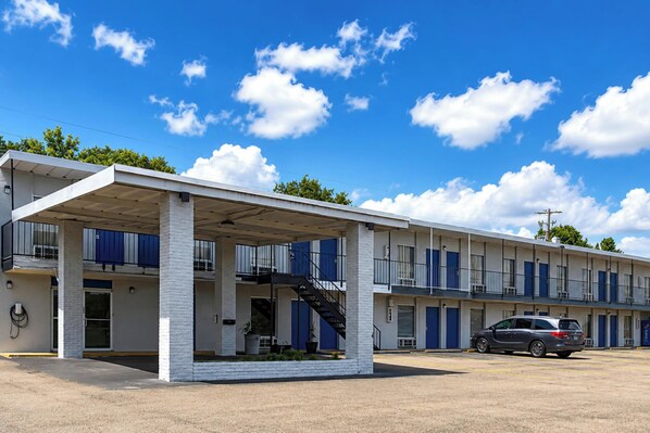 A motel with a covered parking area, multiple rooms, and a staircase leading to the upper level.