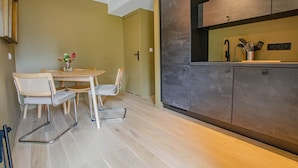 A compact kitchen with a dining area, featuring a round table, two chairs, and a modern cabinet design. - Le Cottage - MAISONS LES CHAOURCE (MAISONS LES CHAOURCE)