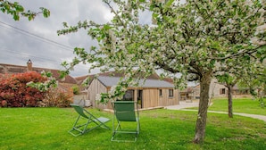 A garden with two green lawn chairs, a wooden shed, and a tree with white blossoms. - Le Cottage - MAISONS LES CHAOURCE (MAISONS LES CHAOURCE)