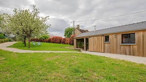 A modern wooden building with a glass door entrance, a paved pathway, and a tree with blooming flowers. - Le Cottage - MAISONS LES CHAOURCE (MAISONS LES CHAOURCE)