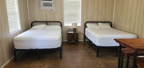 Two single beds with white linens, a small wooden table, and a wall-mounted heater.