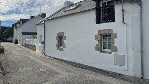 Un bâtiment blanc avec des encadrements de fenêtres en pierre, un toit en pente et une rue étroite.