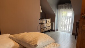 Une chambre à coucher avec un lit, une commode en bois et une fenêtre ornée d’un rideau en dentelle.