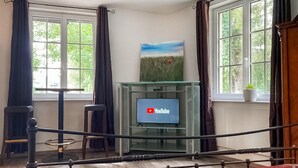 Una stanza con un letto, una TV su un mobile in vetro, un quadro al muro e finestre con tende.