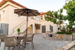 Relax on the stone-tiled patio with a dining set and umbrella, surrounded by lush greenery.