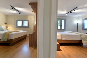 Two single beds with bedside tables, set against a clean and bright backdrop of white walls and wooden floors.