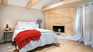 Une chambre à coucher comprenant un lit, une table de chevet, une lampe, une cheminée et une fenêtre avec des rideaux.