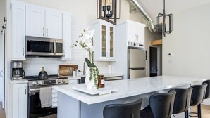 Une cuisine moderne avec des meubles blancs, des appareils en acier inoxydable, un îlot central doté de tabourets et une plante décorative, une orchidée.