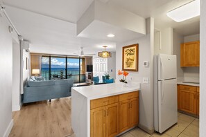 Una cocina moderna con armarios de madera, un refrigerador blanco y un comedor con vista al océano.