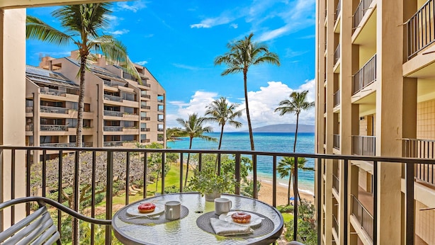 Un balcon avec une table et des chaises, donnant sur une plage et des palmiers.