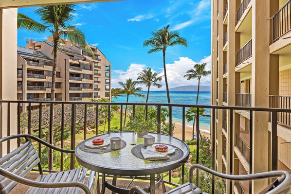 A balcony with a table and chairs, overlooking a beach and ocean.