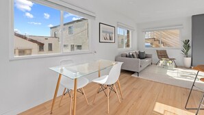 Una sala de estar moderna con una mesa de comedor de vidrio, sillas blancas, un sofá gris y una escalera que sube a un piso superior.