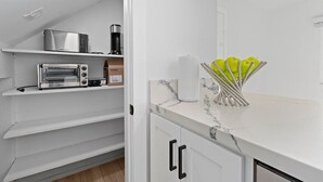 Una cocina con muebles blancos, encimera de mármol, tostadora, cafetera y un bloque de cuchillos.